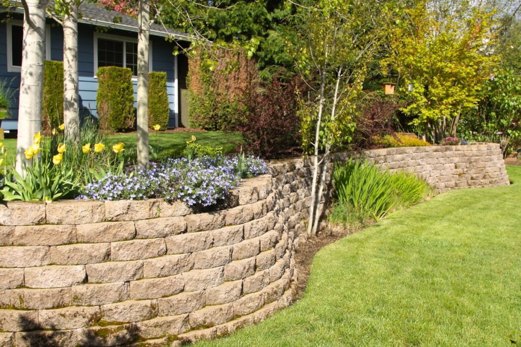 A landscaping project featuring a retaining wall amidst a lush yard filled with grass and flowers.