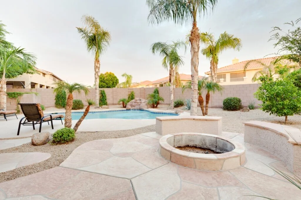 A backyard patio with a fire pit and palm trees.