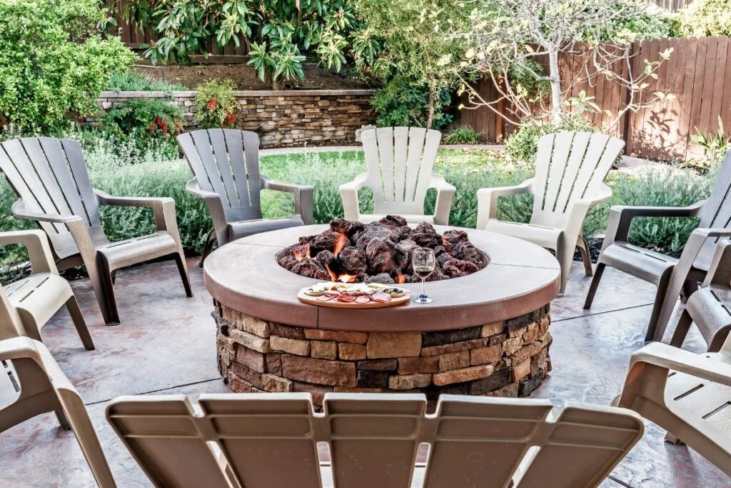 A fire pit in a backyard patio with chairs around it.