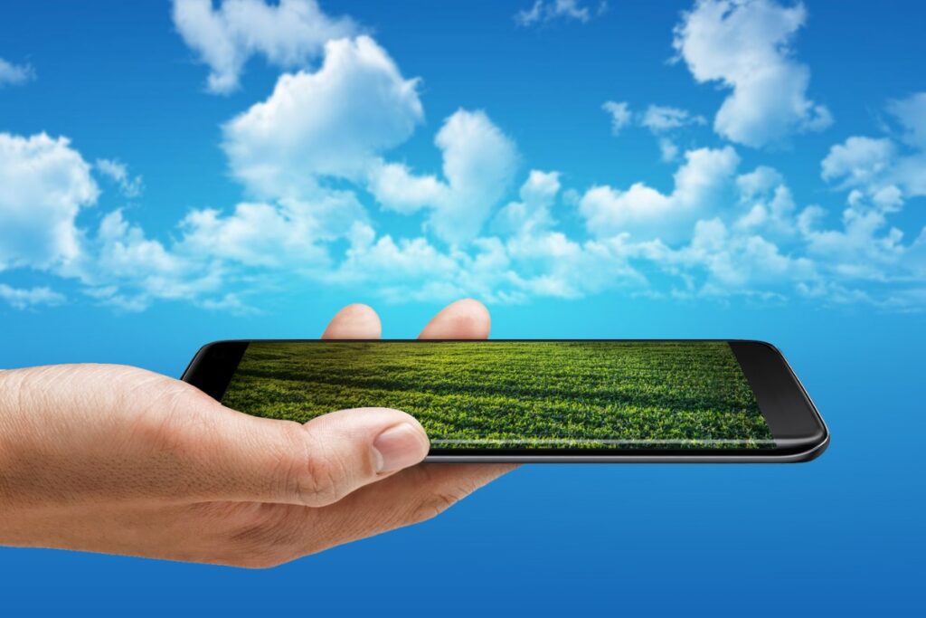 A hand holding a smart phone with a green field in the background, showcasing the latest Landscape Architecture Trends.