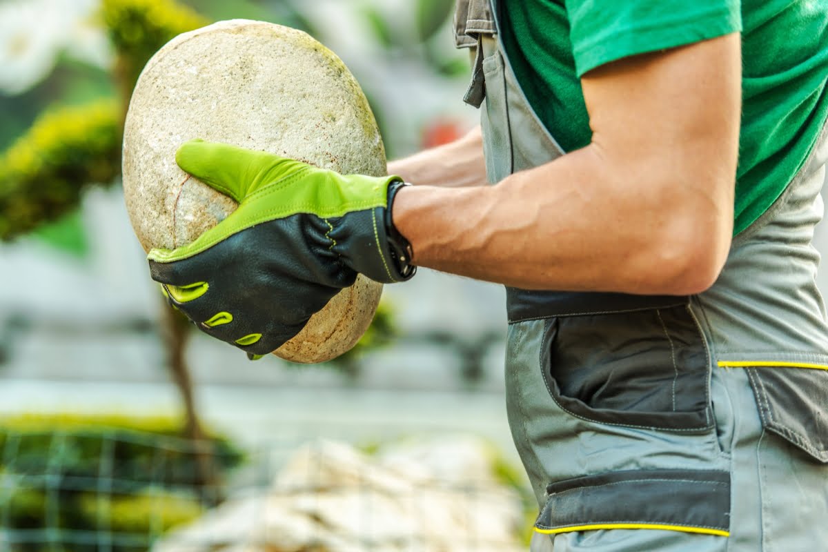 A man in overalls is holding a boulder in his hands.