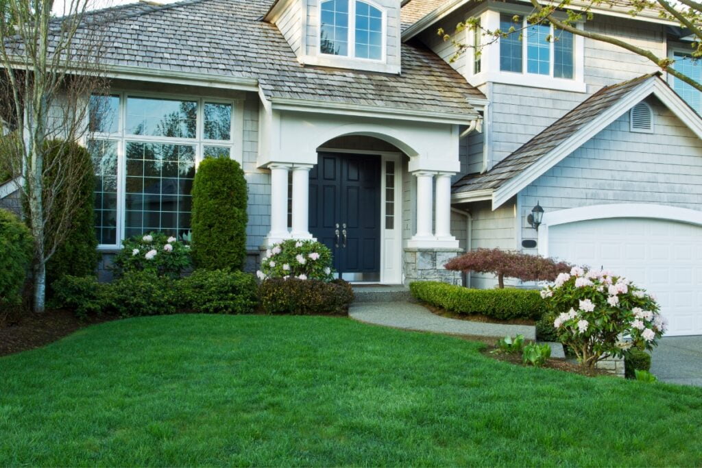 A front yard landscape design featuring a house with a lawn and bushes.