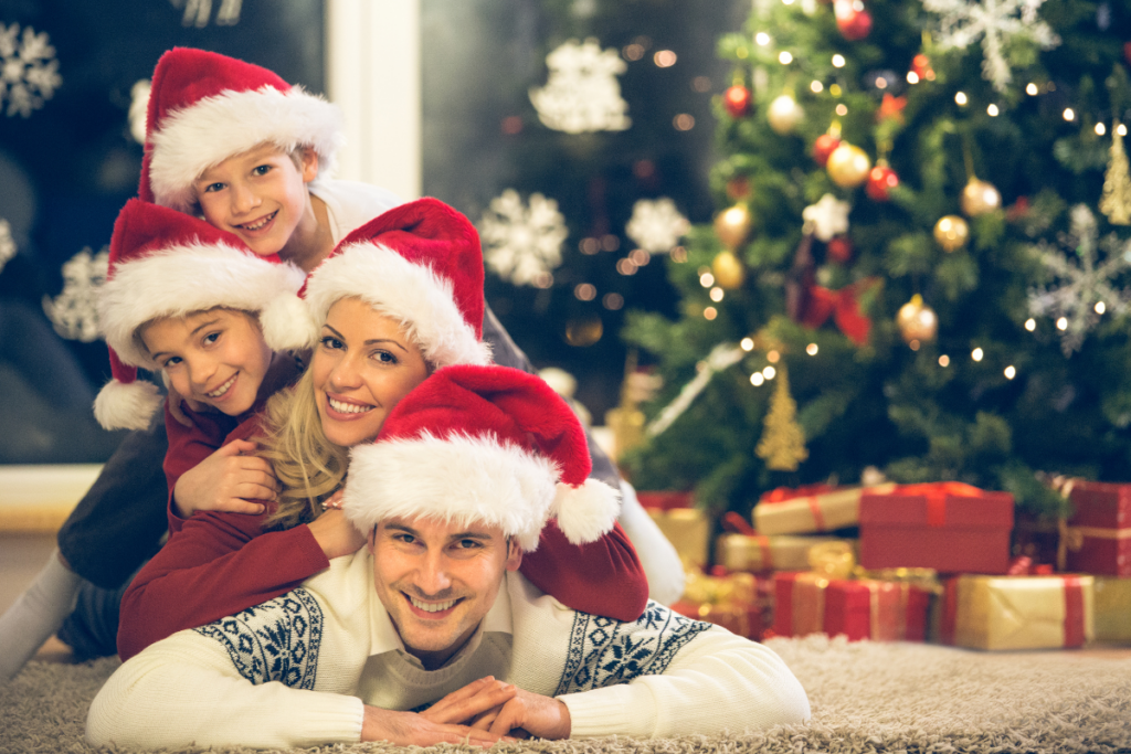 A family in Santa hats gathered on the floor in front of a Christmas tree.
