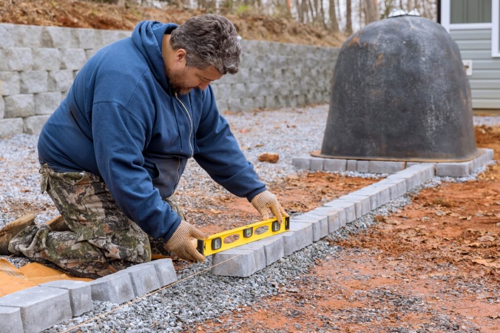 A man using a measuring tape to measure a garden stone border.