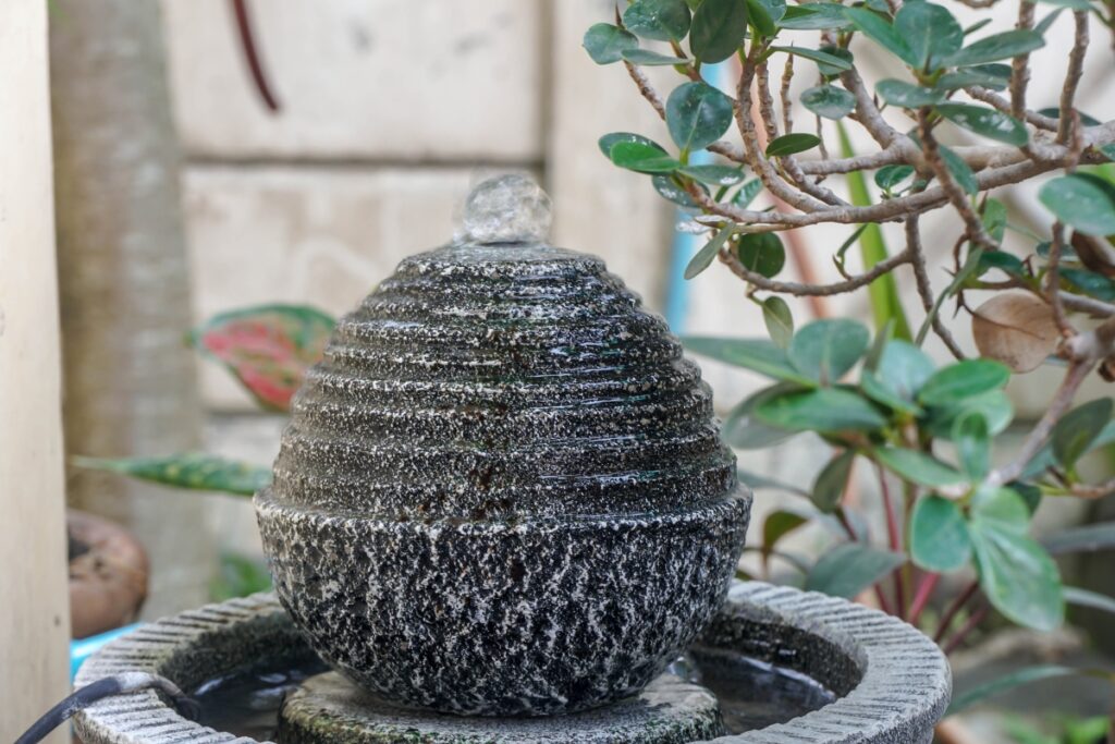 A trendy water fountain in the shape of a beehive sitting on top of a planter.