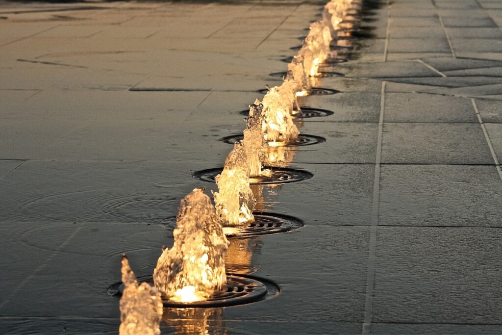 A line of water fountains on a sidewalk, showcasing the latest water feature trends at dusk.