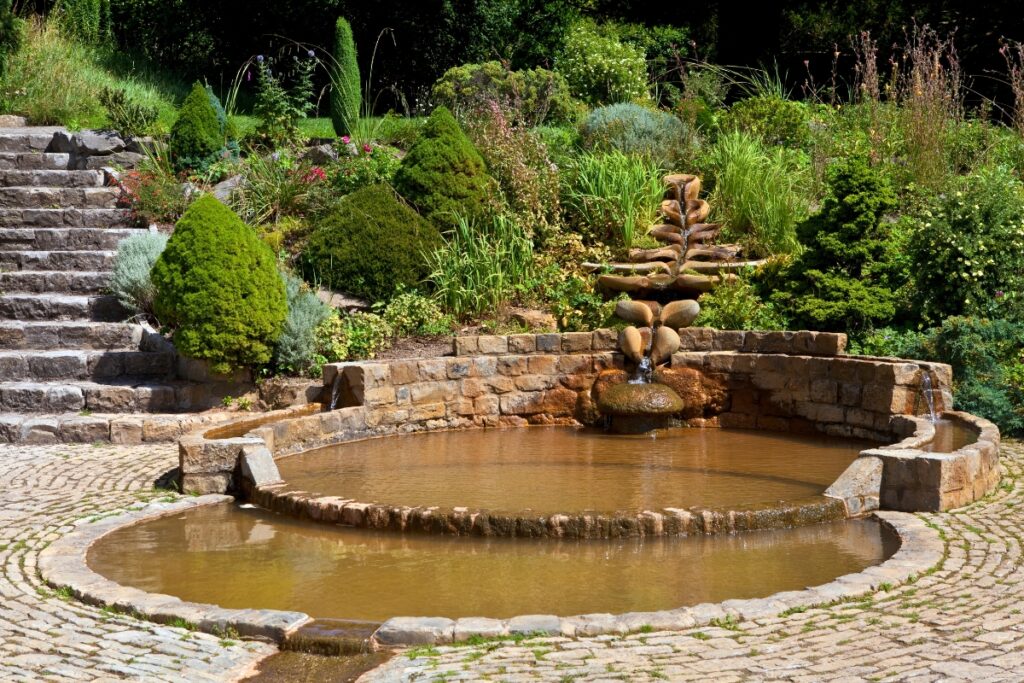 A stone fountain with cascading water, emblematic of outdoor living trends, surrounded by a well-manicured garden and stone steps.