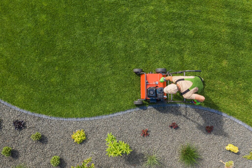 A person is mowing a lawn with a lawn mower, following the yard grading.