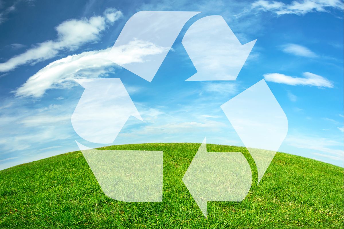 Recycling symbol overlaying a scenic view of eco-friendly landscaping on a green hill under a clear blue sky, representing environmental conservation.