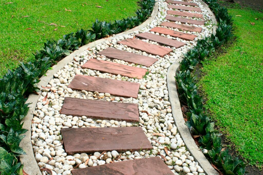 Curved garden path, a hardscape design with red stepping stones and white pebbles surrounded by green grass.