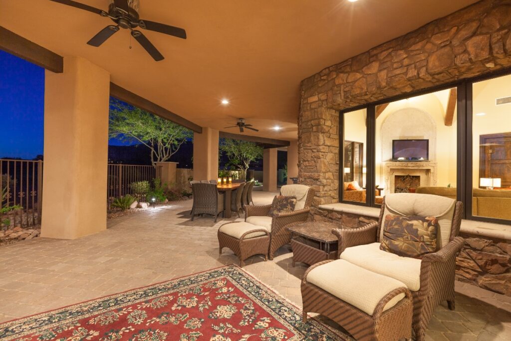 Spacious covered patio area with comfortable seating, a hardscape design fireplace, and a view of the outdoor landscape at dusk.