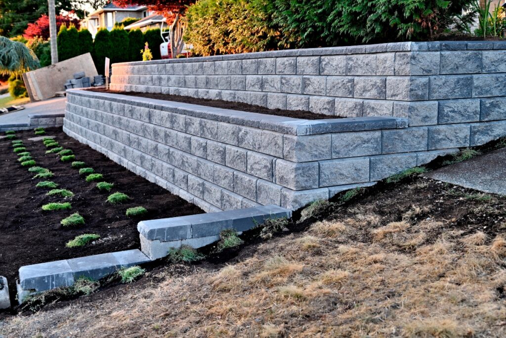 Newly constructed retaining wall made of interlocking stone blocks with a freshly landscaped garden bed in a residential area, incorporating hardscape design.
