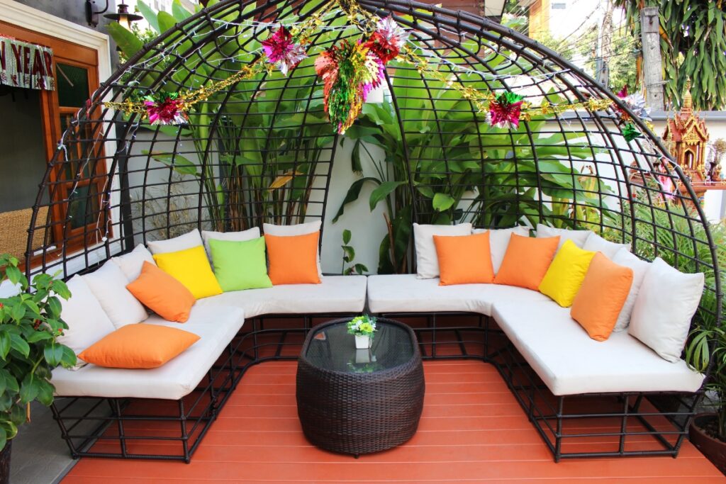 An outdoor seating area with colorful cushions under a dome-shaped trellis adorned with flowers, integrated into a hardscape design.