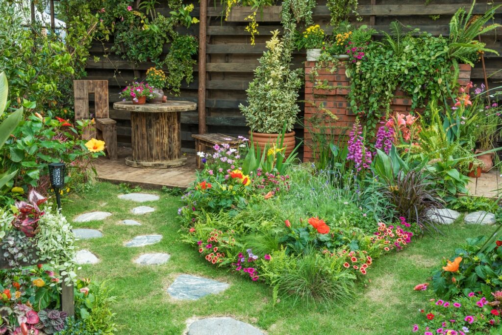 Lush wildlife-friendly landscaping garden with colorful flowers, a wooden deck with seating, stepping stones, and decorative brick walls.