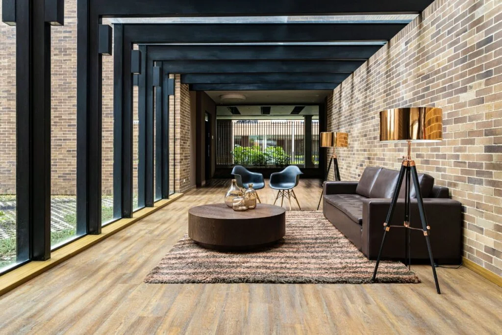 Atlanta Outdoor Living Spaces Transformed into Tranquil Backyard Retreats 8 A modern lounge area with a brown sofa, round coffee table, two black chairs, two floor lamps, and brick walls features large windows on the left side that let in ample natural light, reminiscent of Atlanta outdoor living spaces.