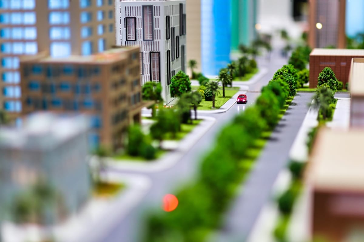 A miniature model of a city showcases high-rise buildings, lush community green spaces, and a red car on the road.