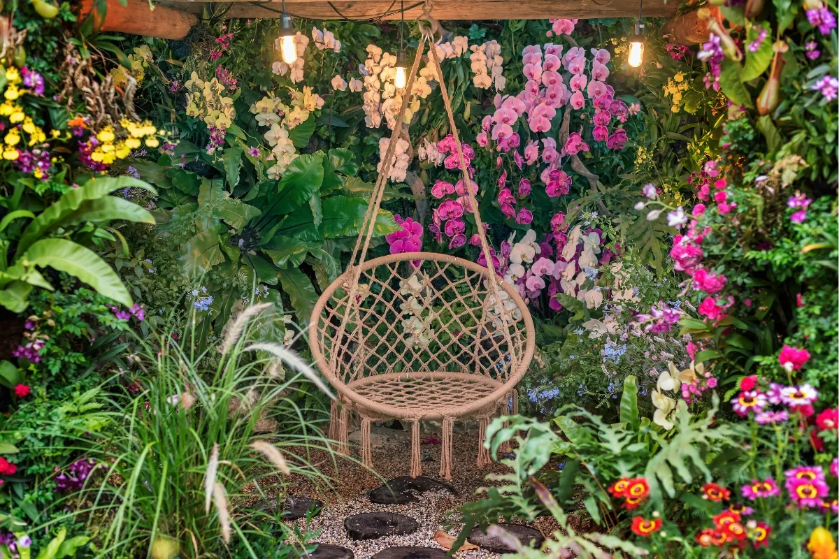 Outdoor Makeovers: Transform Your Yard with Elegant Landscaping & Hardscaping 4 A wicker hanging chair graces the lush garden, a testament to outdoor makeovers, surrounded by vibrant flowers and foliage under twinkling hanging lights.