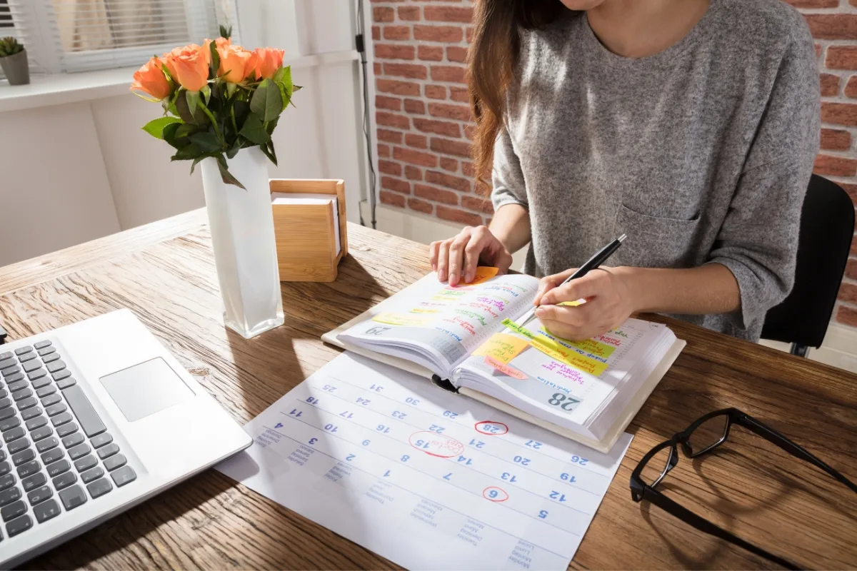 Front Yard Makeover: Transform Your Home With Low-Maintenance Landscaping Ideas 1 Amidst a vase of roses, someone meticulously plans their front yard makeover, surrounded by a laptop and calendar sheet at a neatly organized desk.
