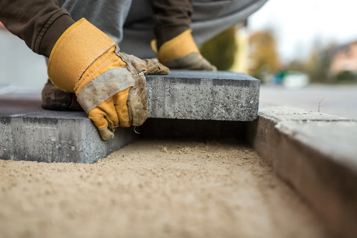 Wearing yellow gloves, a person skillfully demonstrates how to lay pavers on a perfectly prepared bed of sand.