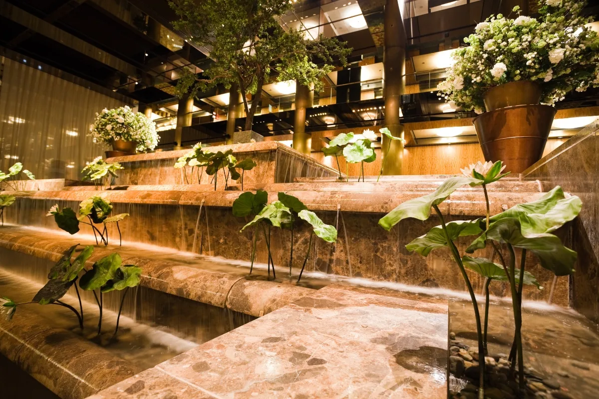 Commercial Water Features in Smyrna: How They Help Attract More Customers 2 Marble tiered commercial water feature with green plants and large floral arrangements, set in a modern, well-lit indoor space.