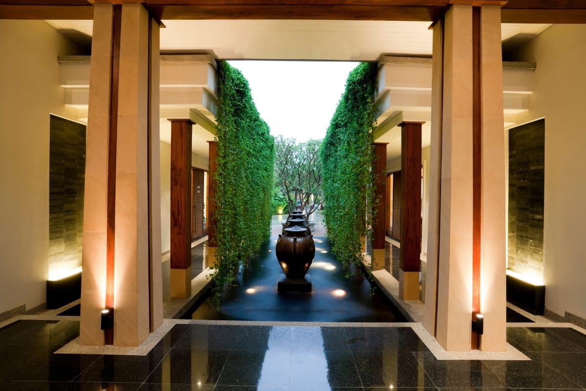 Commercial Water Features in Smyrna: How They Help Attract More Customers 3 A symmetrical corridor with tall columns, hanging greenery, large black vases, and soft lighting leads to an outdoor garden area featuring elegant commercial water features.
