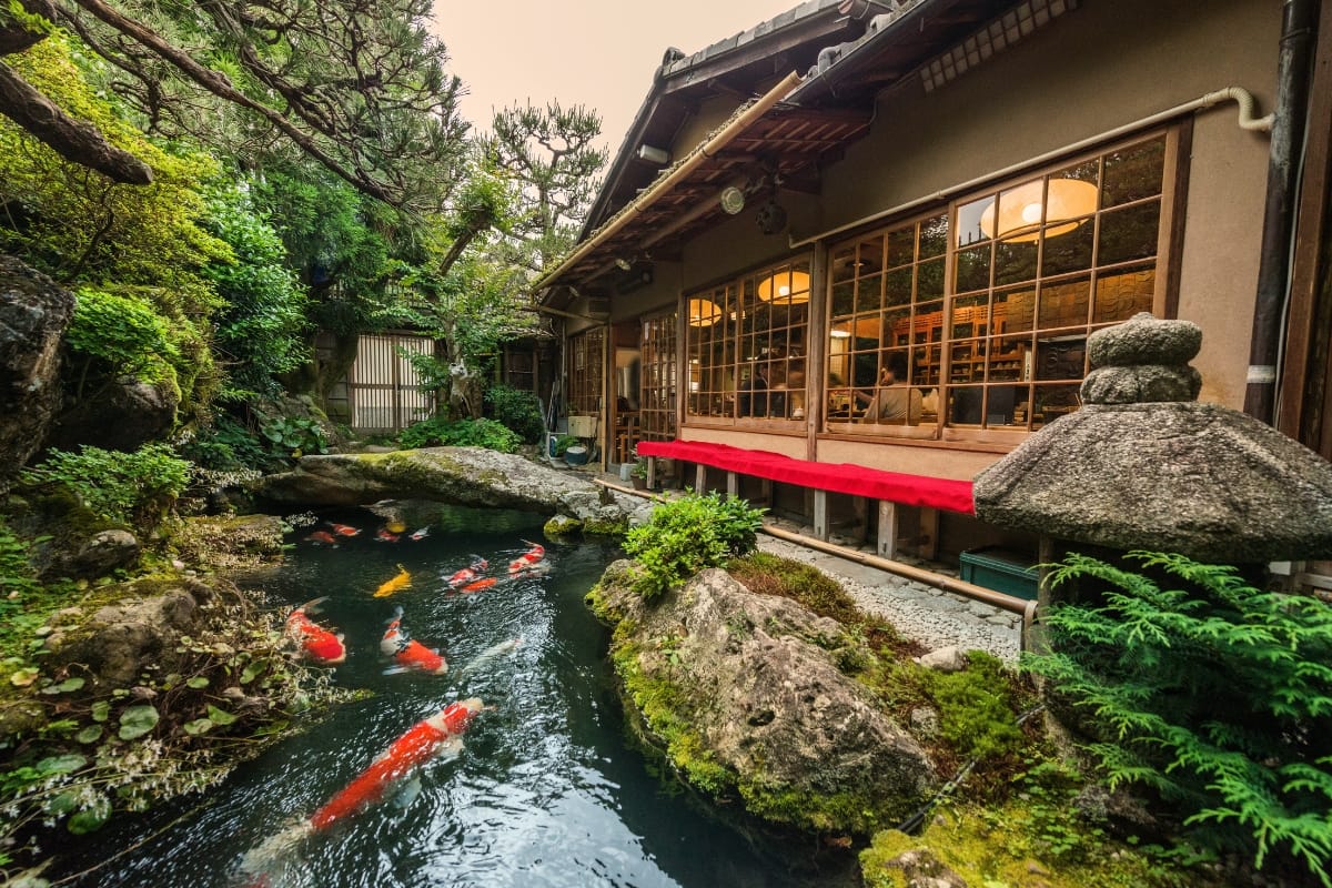 Commercial Water Features in Smyrna: How They Help Attract More Customers 1 A traditional Japanese house overlooks a koi pond surrounded by greenery, with sliding wooden doors and outdoor lanterns visible—an inspiring blend of serene design and commercial water features.