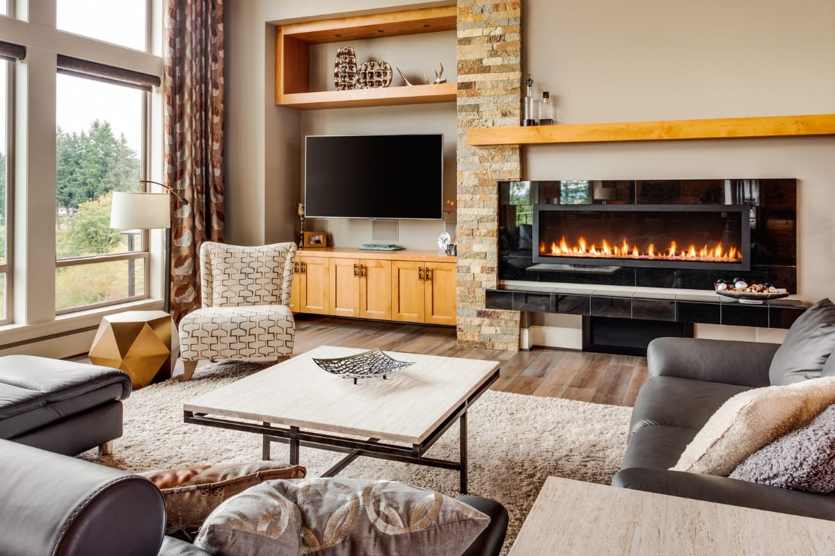 Fire Features in Buckhead: Why Commercial Spaces Should Invest 3 Modern living room with a wall-mounted TV, striking fire features including an electric fireplace, stone accents, leather sofas, large windows, and a coffee table on a beige rug.