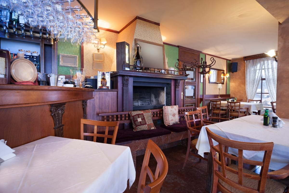 Fire Features in Buckhead: Why Commercial Spaces Should Invest 7 A cozy restaurant interior with wooden chairs, tables covered in white cloths, elegant fire features by the fireplace, and warm decorative lighting.