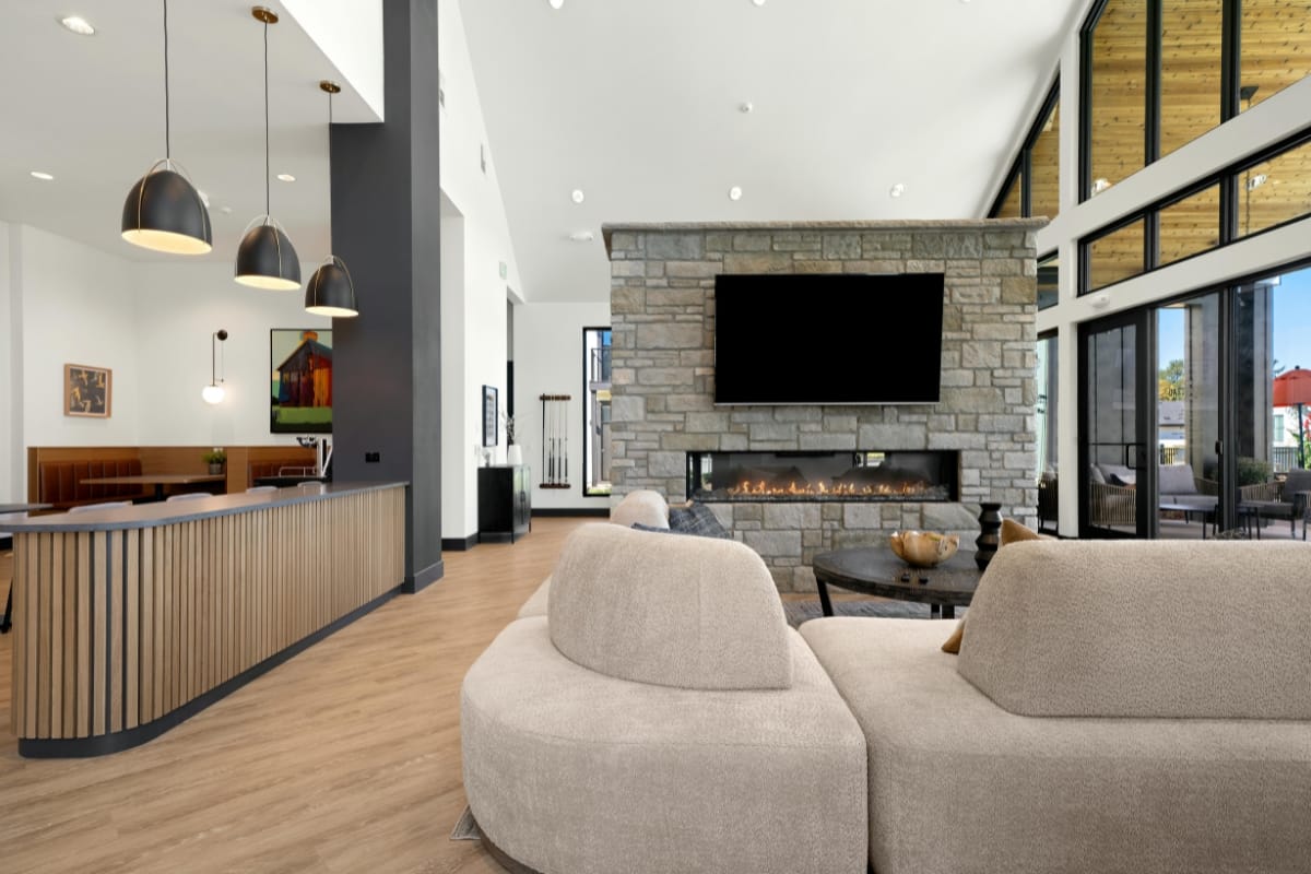 Fire Features in Buckhead: Why Commercial Spaces Should Invest 8 Modern living room with beige curved sofas, stone fireplace fire feature, wall-mounted TV, and large windows; adjacent open kitchen area with pendant lights and wood accents.
