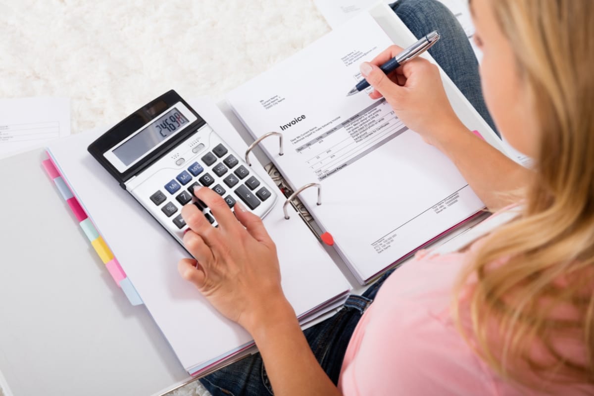 Rain Gardens in Marietta: Boosting Commercial Property Value with Professional Design 9 A person uses a calculator and reviews an invoice in a binder, writing with a pen. Nearby, folders with colored tabs organize documents about rain gardens.