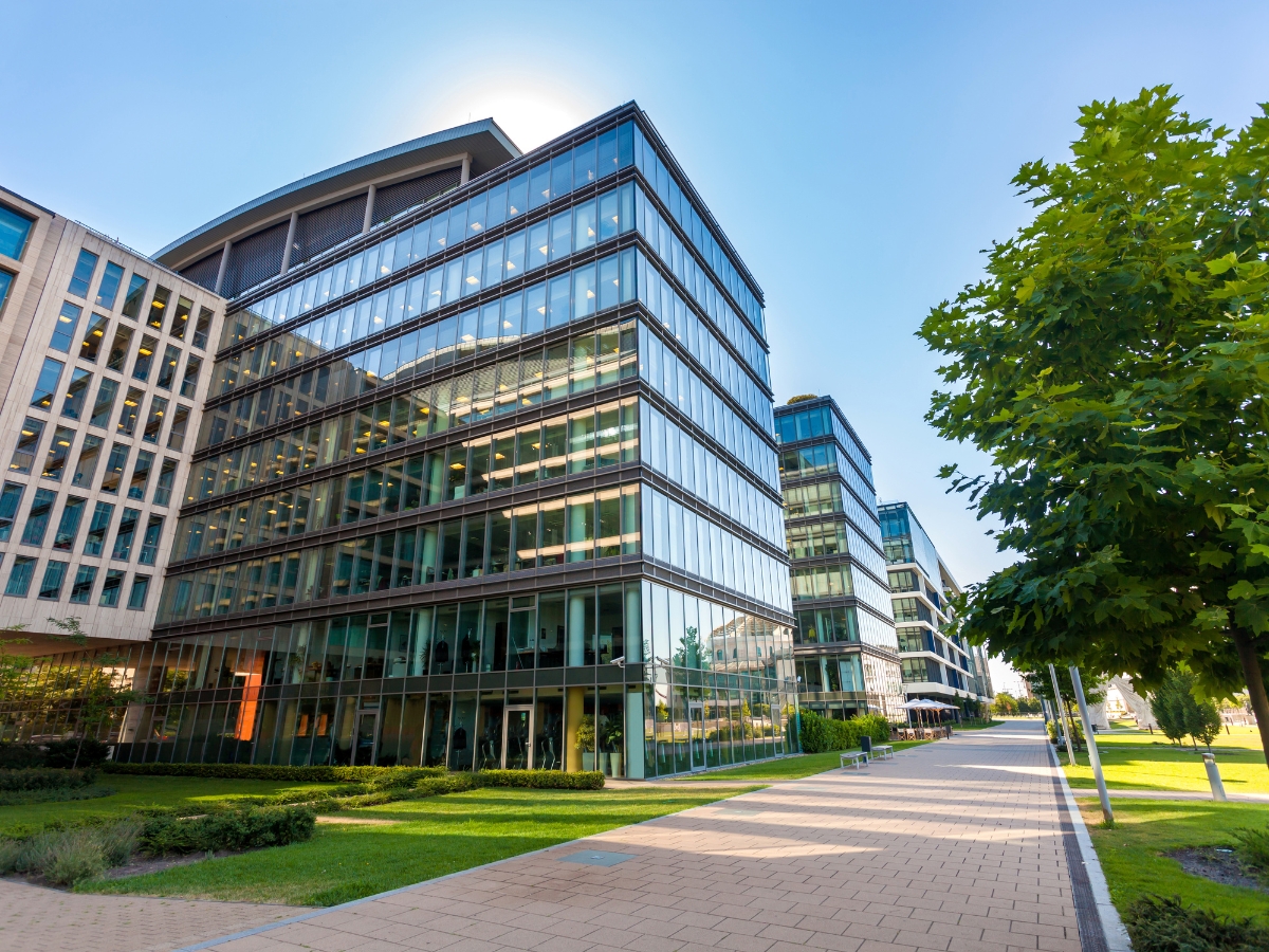 Modern glass office buildings with multiple floors, surrounded by green trees and expertly designed year-round hardscaping in Alpharetta, all set beneath a clear blue sky.