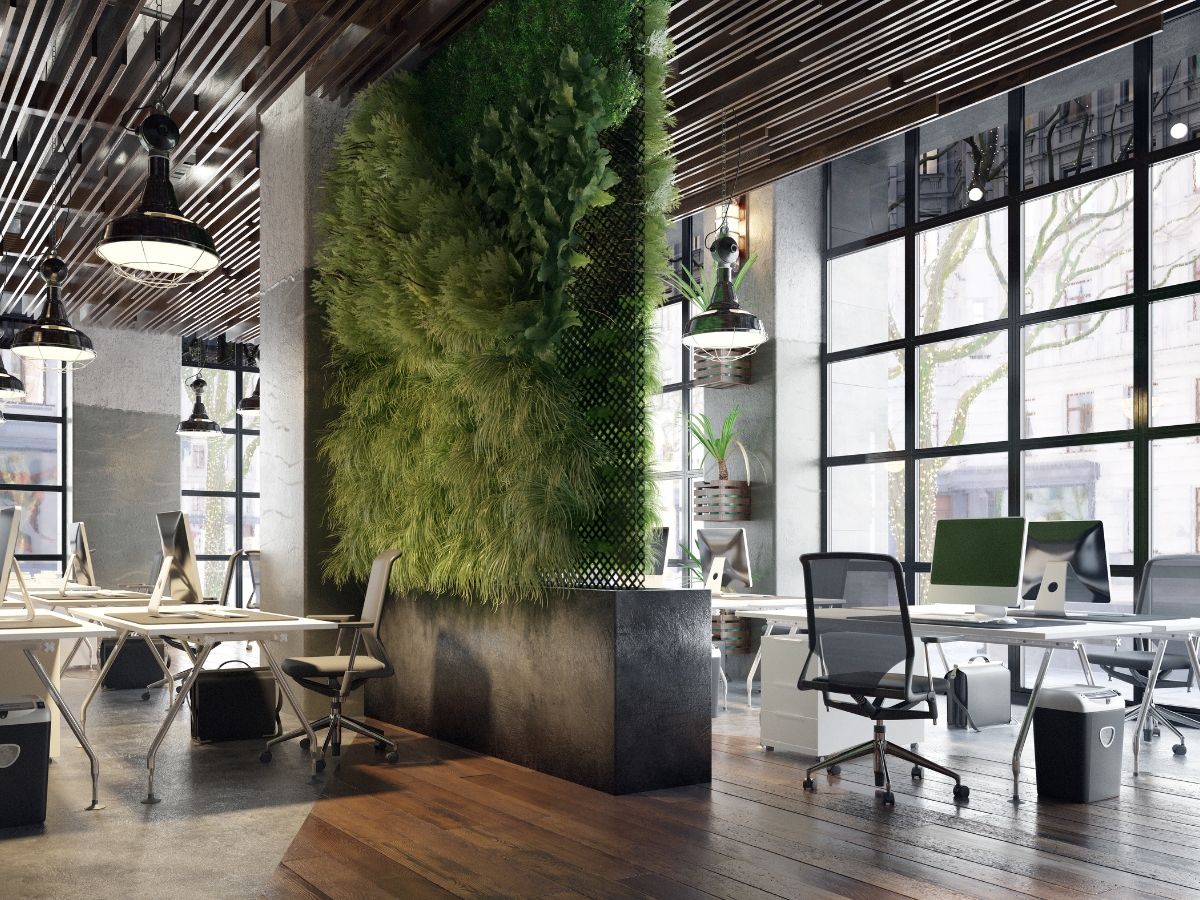 Modern open-plan office with large windows, several desks and chairs, and a vertical green plant wall dividing the workspace—perfect inspiration for year-round hardscaping in Alpharetta.