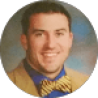 A man with short dark hair is wearing a beige suit, blue shirt, and yellow bow tie, smiling in a posed photograph against a blurry backdrop, as if ready to give glowing testimonials.