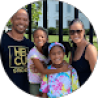 A family of four poses and smiles for a photo outdoors, standing in front of a fence with a building visible in the background—just like you'd see in glowing testimonials.